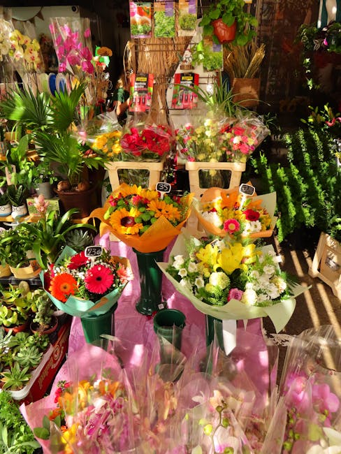 A vibrant display of fresh flower bouquets arranged on a pink cloth-covered table inside a florist shop. The bouquets include a mix of colorful flowers such as sunflowers, gerbera daisies, and roses, 